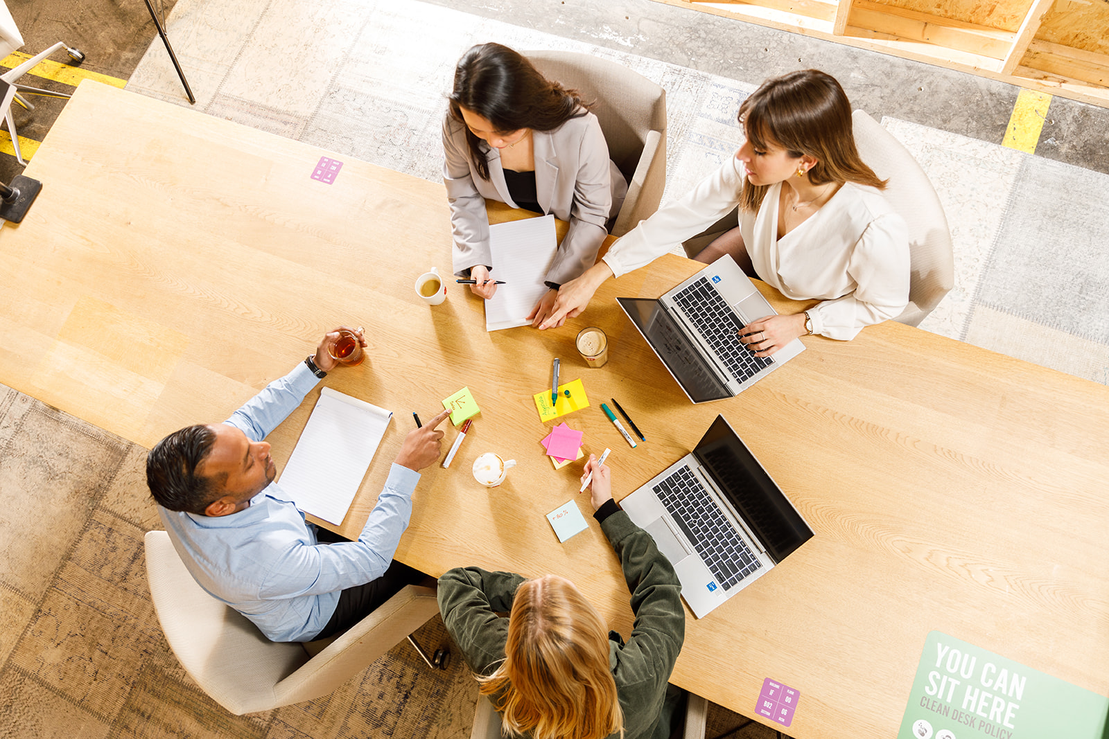 Vier collega’s werken samen aan een tafel met laptops en notities.